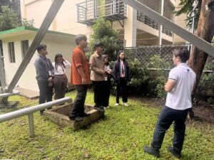 A group of students listens to an instructor in a grassy outdoor area.